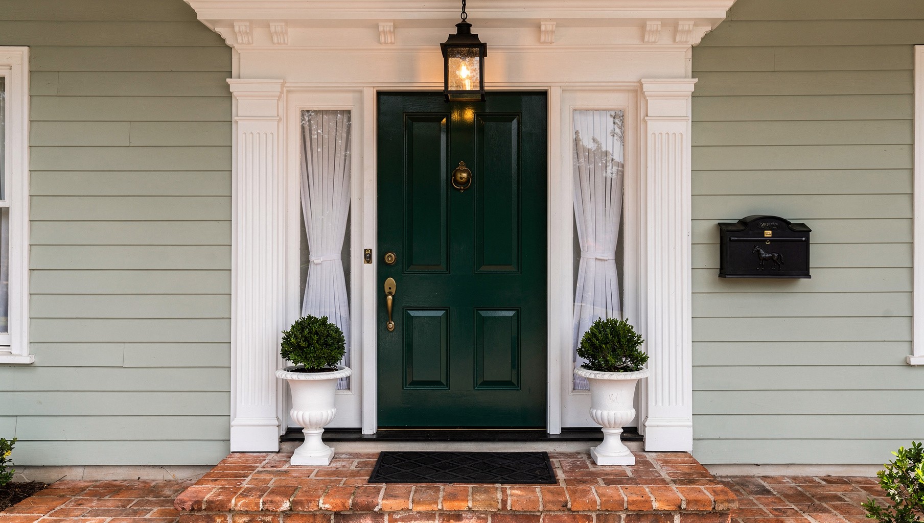 Your front door in matte black with a brass letterbox and house number, set against pale grey render